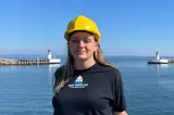 Woman in black t-shirt and yellow helmet in front of lighthouse