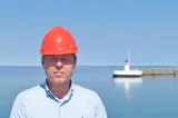 Man in blue shirt and red helmet in front of lighthouse