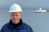 Man in blue jacket and white helmet in front of lighthouse