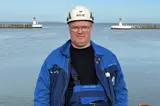 Man in blue jacket and white helmet in front of lighthouse