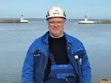 Man in blue jacket and white helmet in front of lighthouse