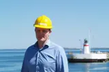 Man in blue shirt and yellow helmet in front of lighthouse