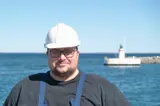 Man in black shirt and white helmet in front of lighthouse